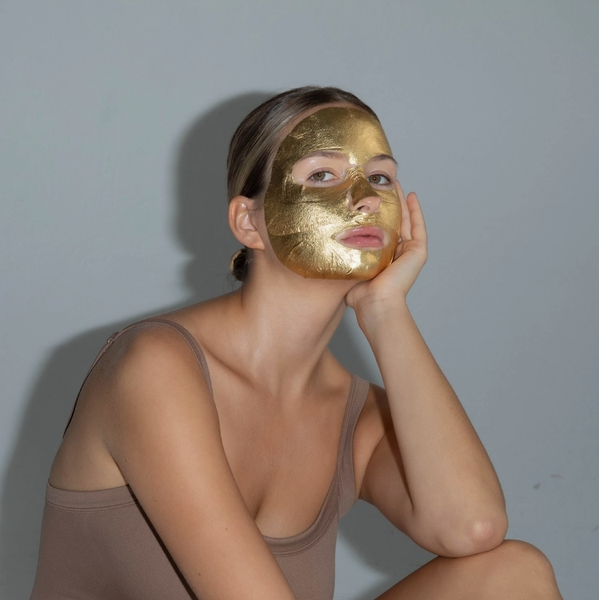 Woman wearing a gold face mask against a plain background