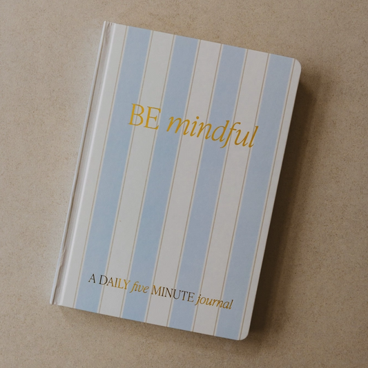 Notebook with blue and white striped cover and 'BE mindful' text on a beige background