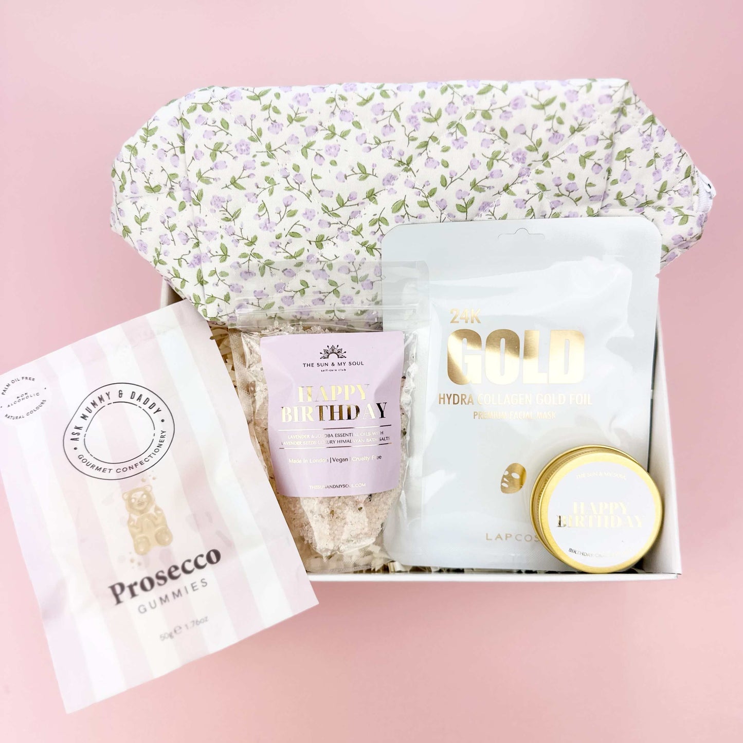 Gift set with floral bonnet, bath salts, and other items on a pink background