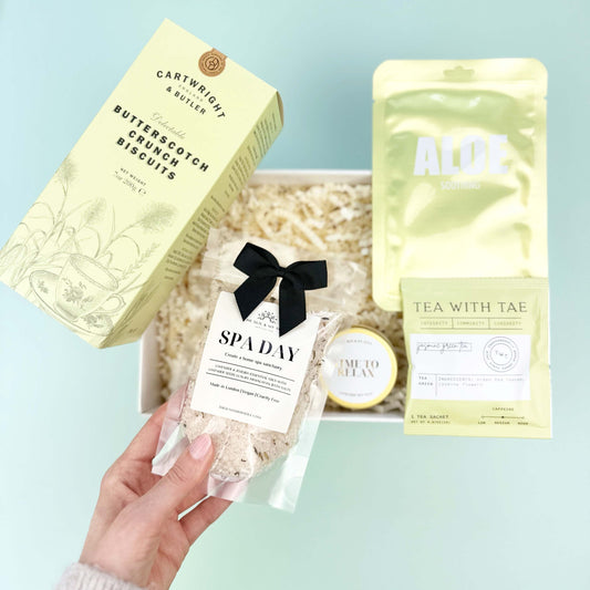 Hand holding a spa day gift set with various items on a light blue surface