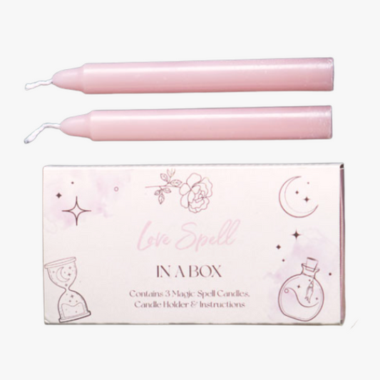 Two pink candles with a box labeled 'Love Spells in a Box' on a white background