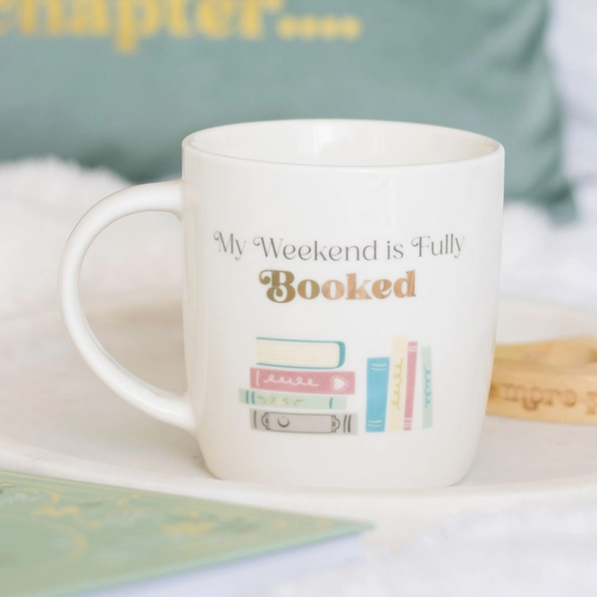 White mug with 'My Weekend is Fully Booked' text and book illustrations on a light background