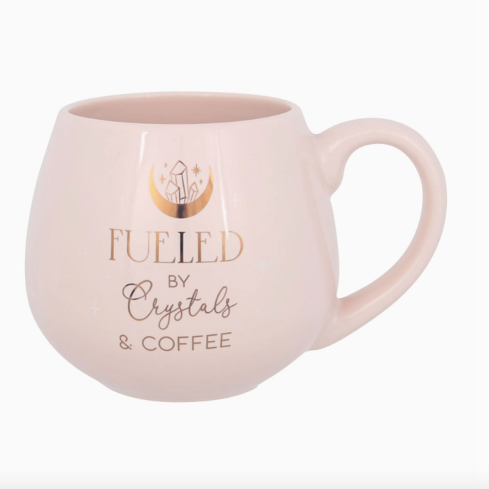 Pink mug with 'Fueled by Crystals & Coffee' text on a white background