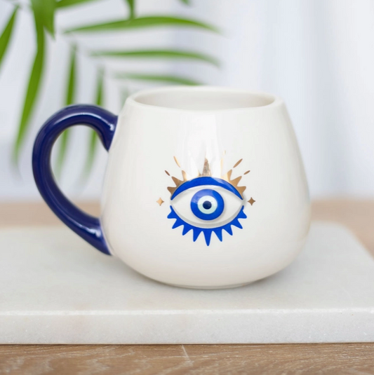 White mug with blue handle featuring an eye design on a white surface with a plant in the background