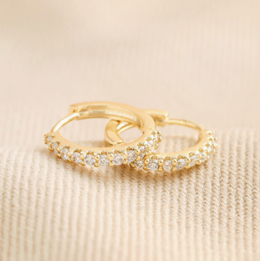 Gold earrings with embedded diamonds on a beige fabric background