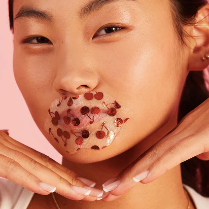 girl with a lip mask featuring red cherries against a pink background