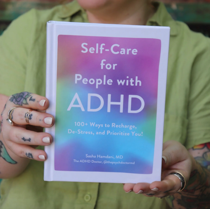 Person holding a book titled 'Self-Care for People with ADHD' with a colorful cover.
