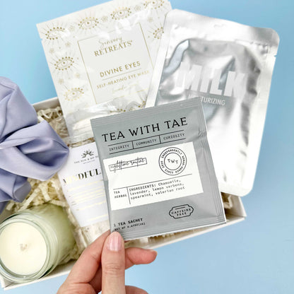 Hand holding a tea bag with 'Tea with Tae' packaging against a light blue background