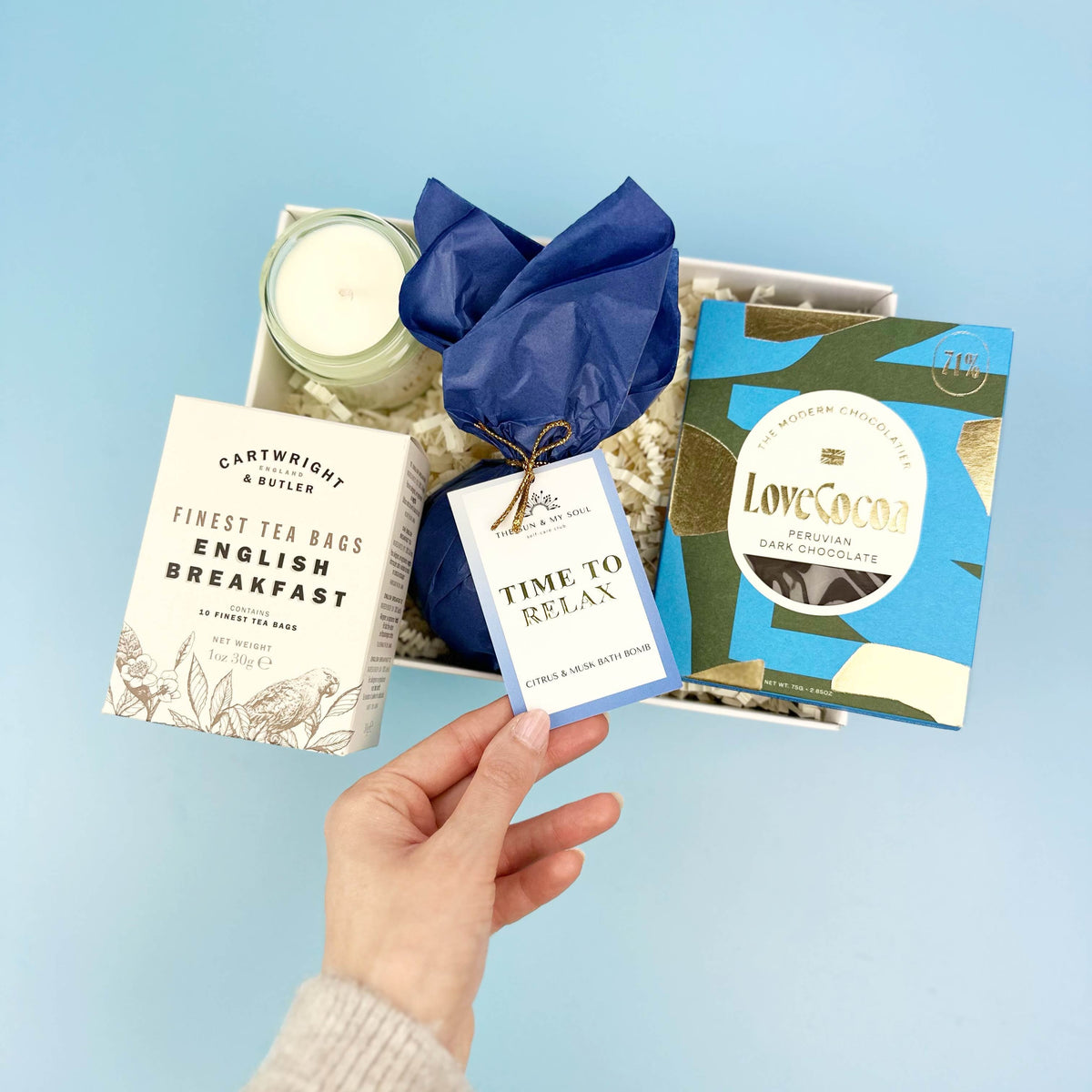 Hand holding a gift card with tea and candle products on a light blue background