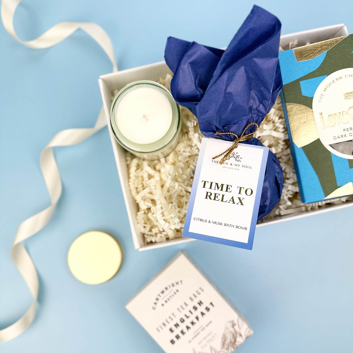 Gift set with candles, bath salts, and a book titled 'Time to Relax' on a light blue background.
