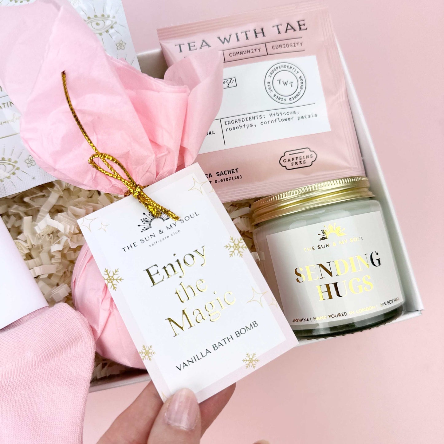 Gift set with candle, tea, and bath bomb on a pink background