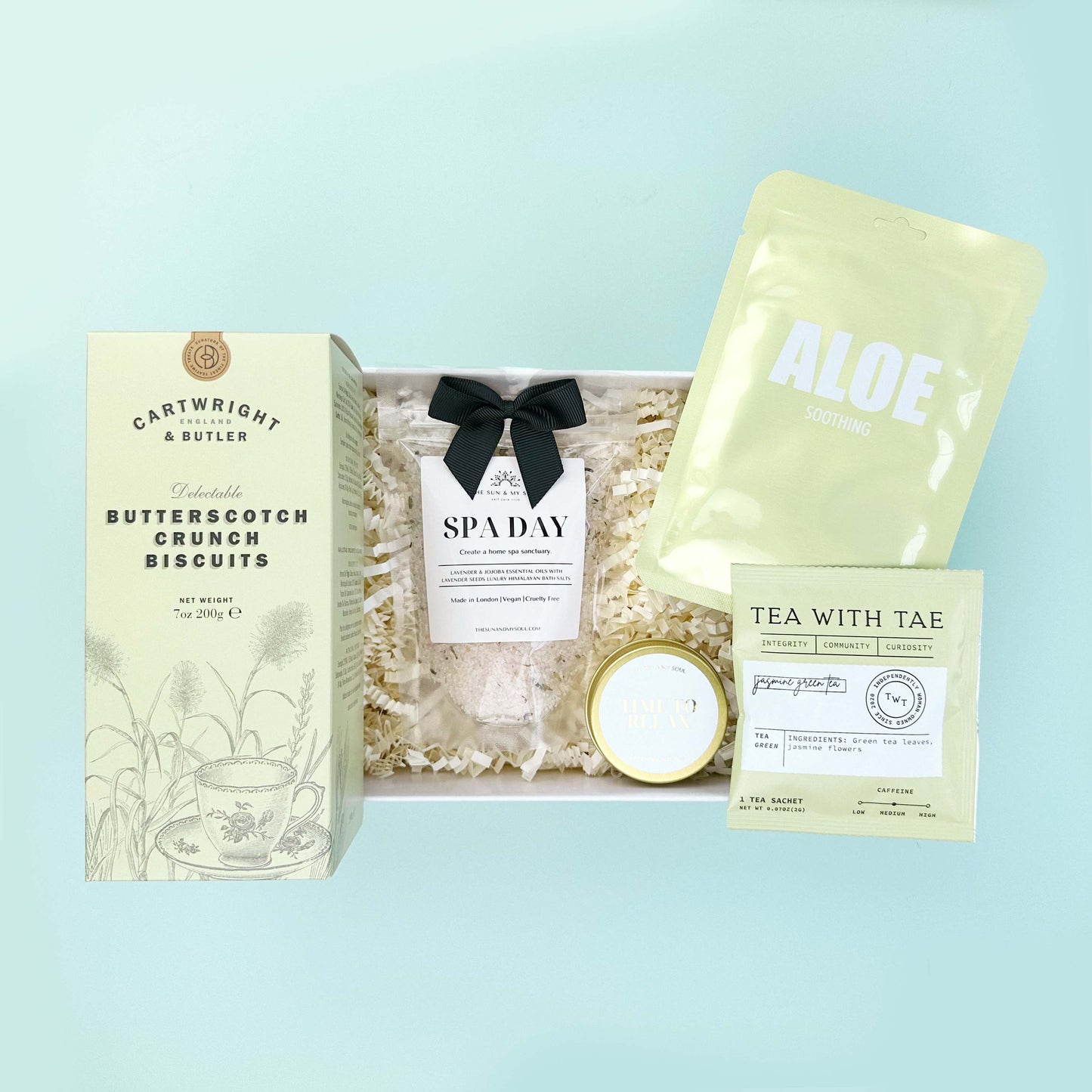 Gift set with Cartwright & Butler butterscotch crunch biscuits, a candle, and tea on a light blue background
