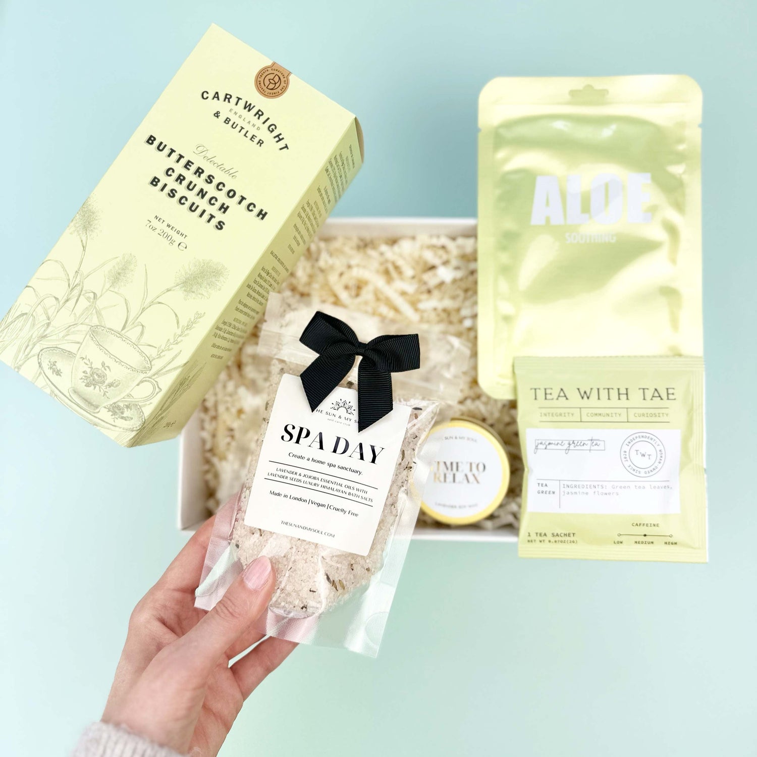 Hand holding a spa day gift set with various items on a light blue surface
