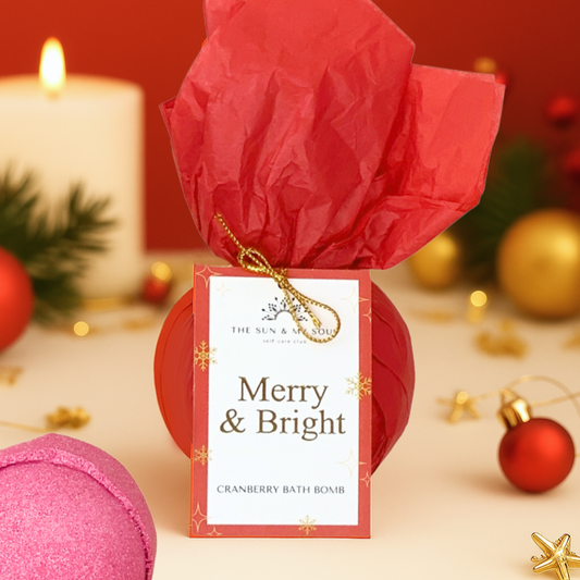 Pink bath bomb with red wrapping and 'Merry & Bright' tag on a festive background