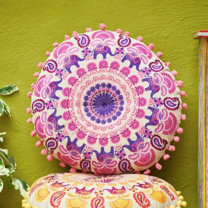 Stack of colorful decorative cushions with intricate patterns on a green wall.