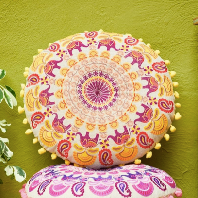 Three colorful mandala-patterned cushions stacked against a green wall.