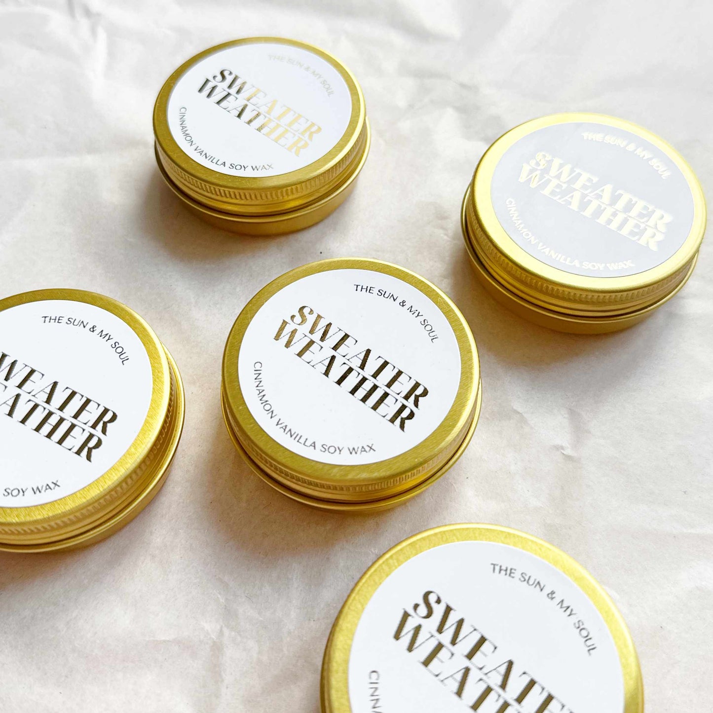 Gold tins labeled 'Sweater Weather' on a white background
