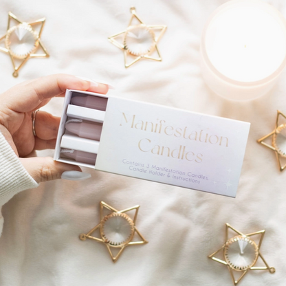Hand holding a box of 'Manifestation Candles' with decorative star-shaped candle holders on a soft surface.