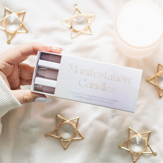 Hand holding a box of 'Manifestation Candles' with decorative star-shaped candle holders on a soft surface.