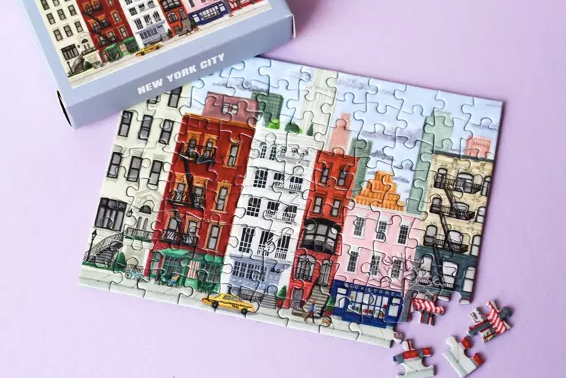 Jigsaw puzzle of New York City buildings with a box on a pink background